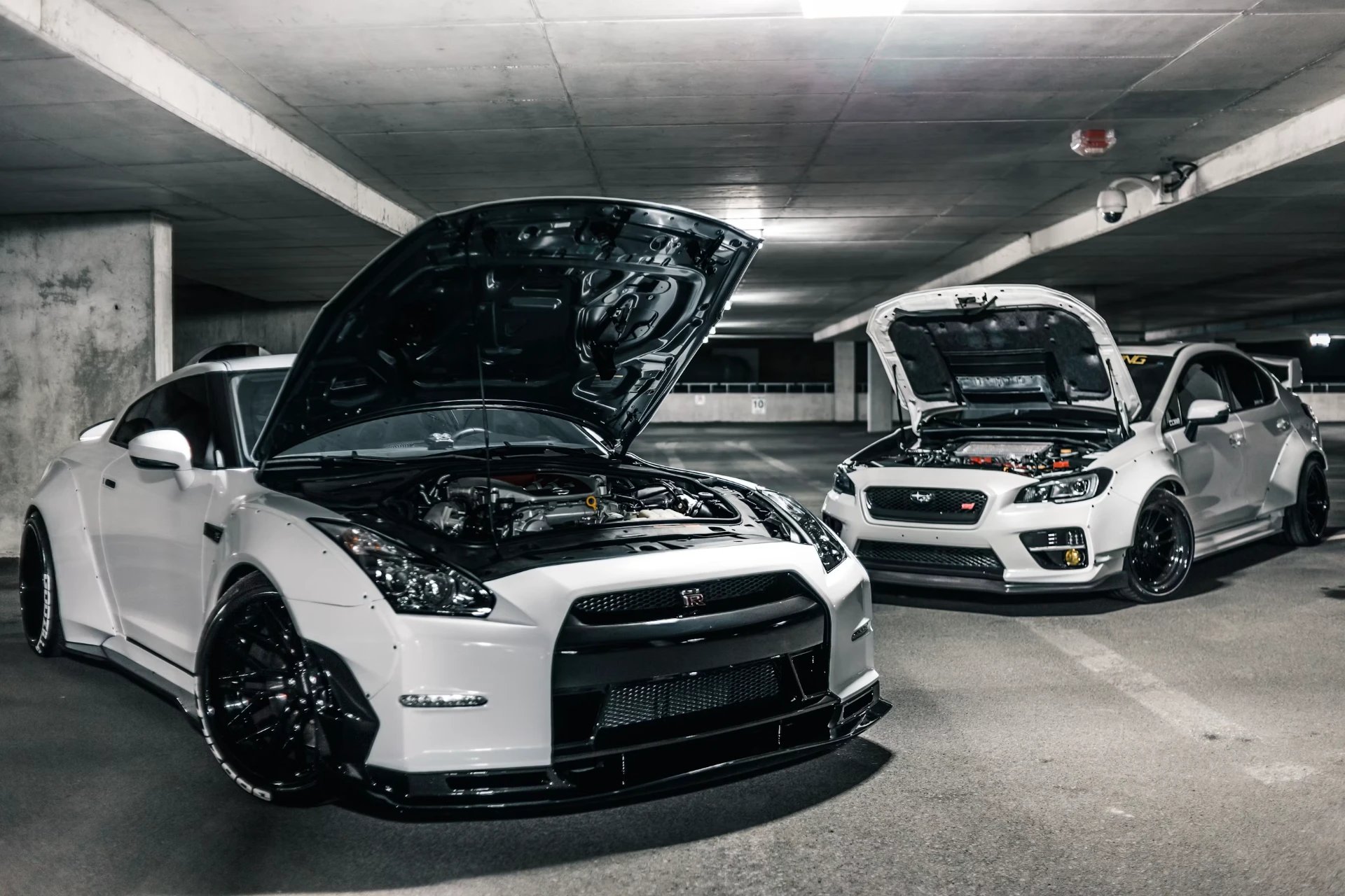 Modified Nissan GT-R and Subaru WRX STI with hoods open in a car park